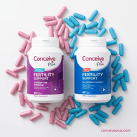 Two Conceive Plus fertility support supplement bottles surrounded by pink and blue capsules on a white background.