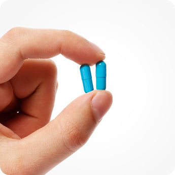 Conceive Plus Men's Fertility Support capsules shown in a close-up held between two fingers, highlighting smooth, bright blue vegan capsule design against white background to emphasize ease of daily use and compact supplement size.