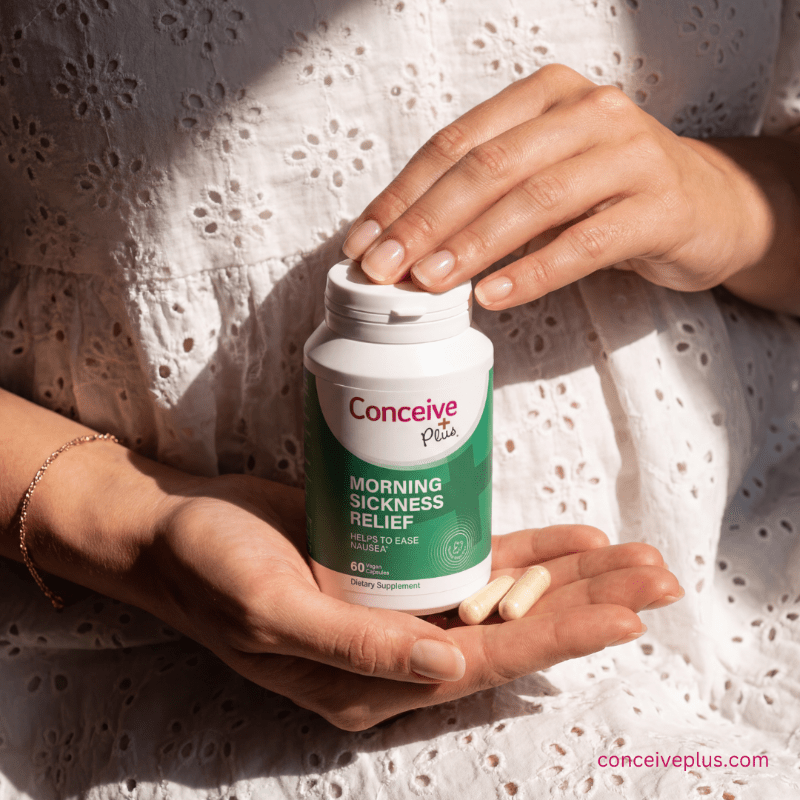 Person holding a bottle of Conceive Plus morning sickness relief supplement with pills in their hand.