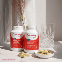 Two bottles of Conceive Plus Motility Support on a table with capsules and a vase in the background.