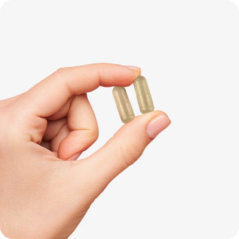 Conceive Plus Ovulation Support vegan capsules shown being gently held between two fingers, highlighting their compact size and easy-to-swallow form against white background.