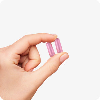 Conceive Plus Women's Fertility Support pink vegan capsules shown between thumb and index finger, highlighting compact size and smooth texture of daily supplement designed to support female fertility health.