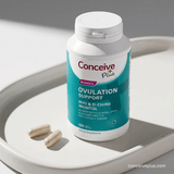 Supplement bottle labeled 'Conceive Plus' on a white surface with two capsules beside it.